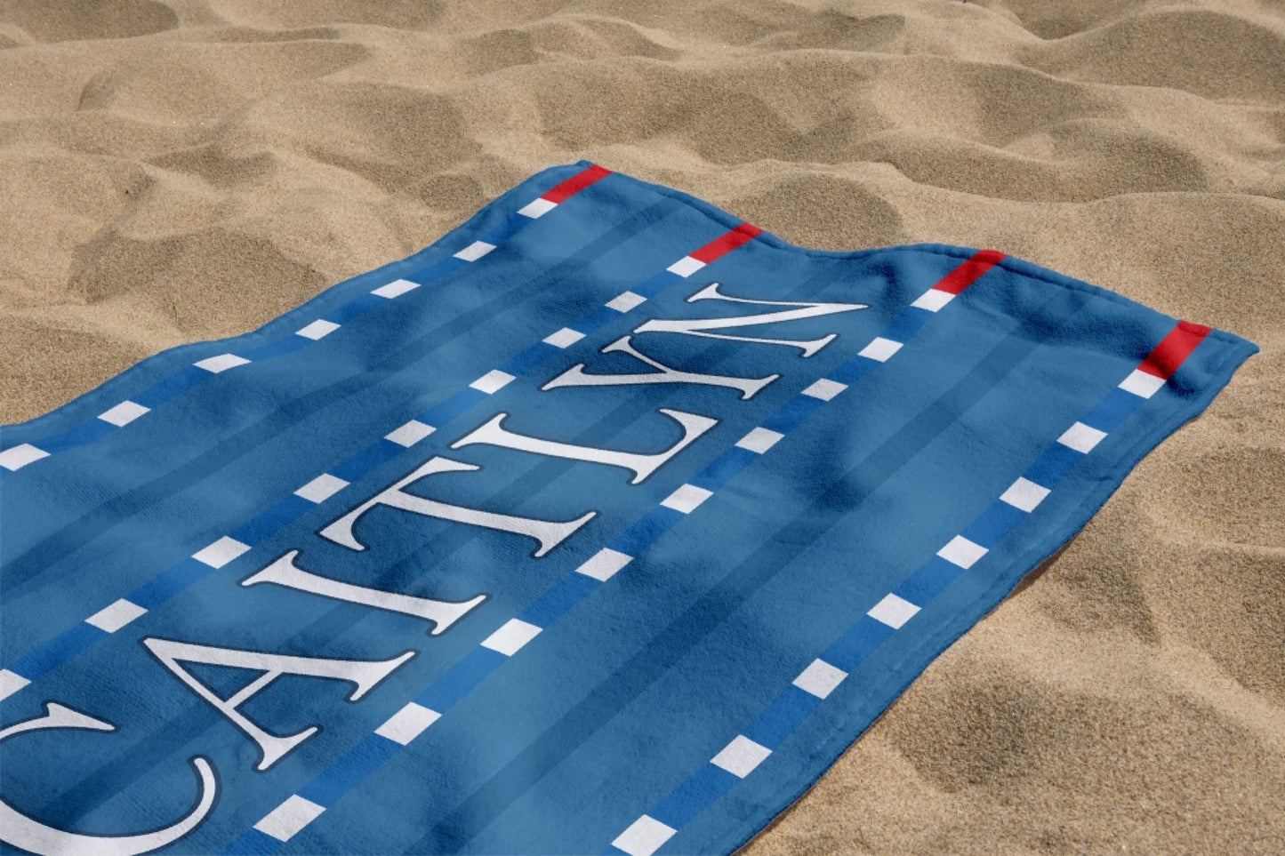 A customized blue beach towel with the name Caitlyn in white font, featuring a striped swimming pool lane design.