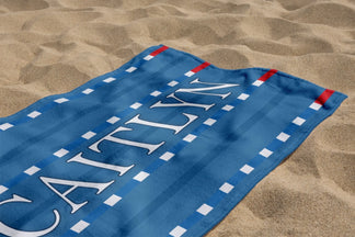 A customized blue beach towel with the name Caitlyn in white font, featuring a striped swimming pool lane design.