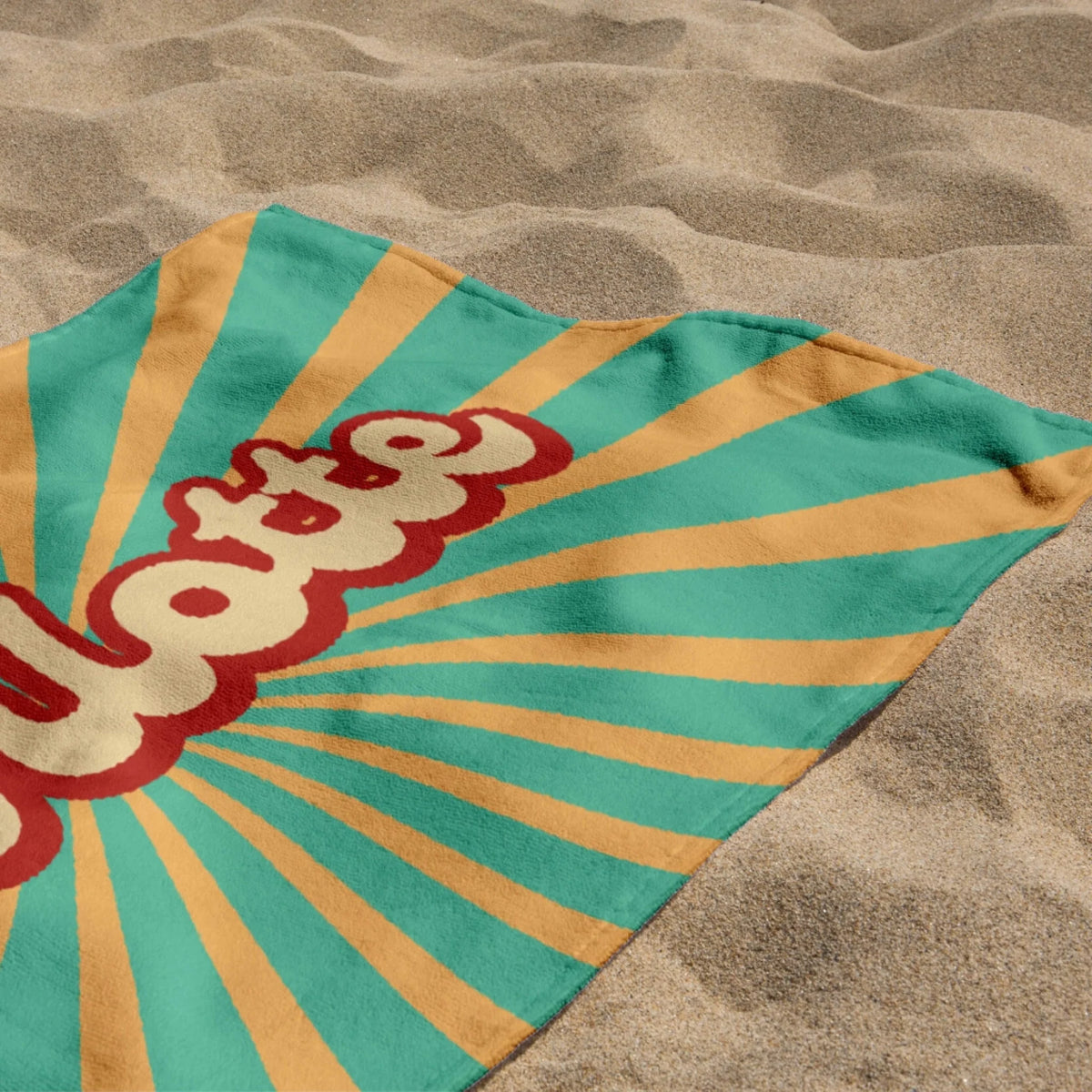 A folded custom beach towel with the name Charlotte and a retro sunburst graphic placed on a sunlit sandy beach.