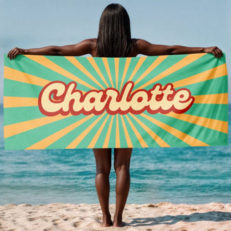 A custom beach towel featuring the name Charlotte in a retro script font over a green and yellow sunburst pattern.