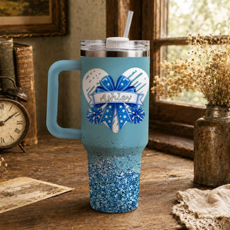 Personalized blue tumbler with glitter base, heart bow design, and custom name Ashley, perfect for cheerleaders.