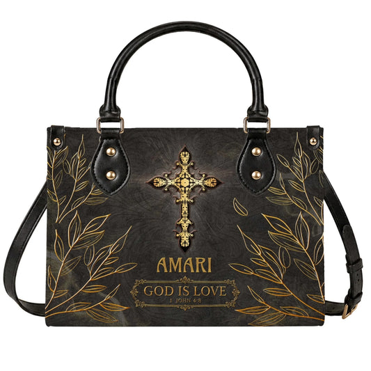A stylish black leather tote bag featuring a gold decorative cross with the name Amari and the quote God is Love 1 John 4:8.