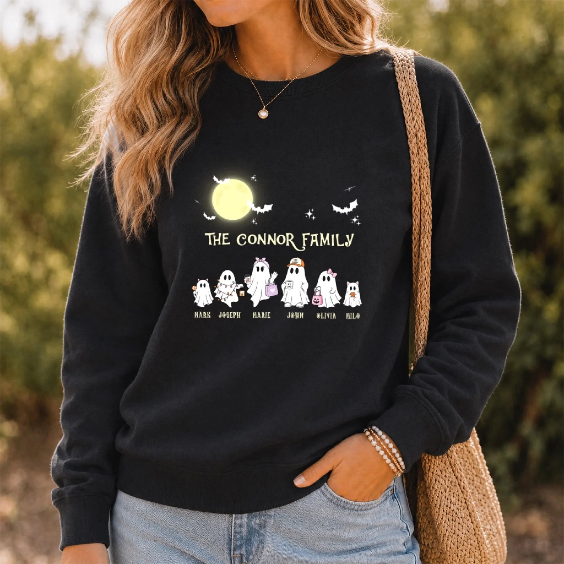 A woman wears a black personalized Halloween sweatshirt featuring a custom ghost family design with individual names.