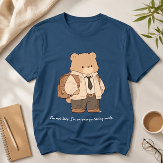 Blue t-shirt with a bear graphic and text, placed on a surface with a notebook, coffee cup, and glasses.