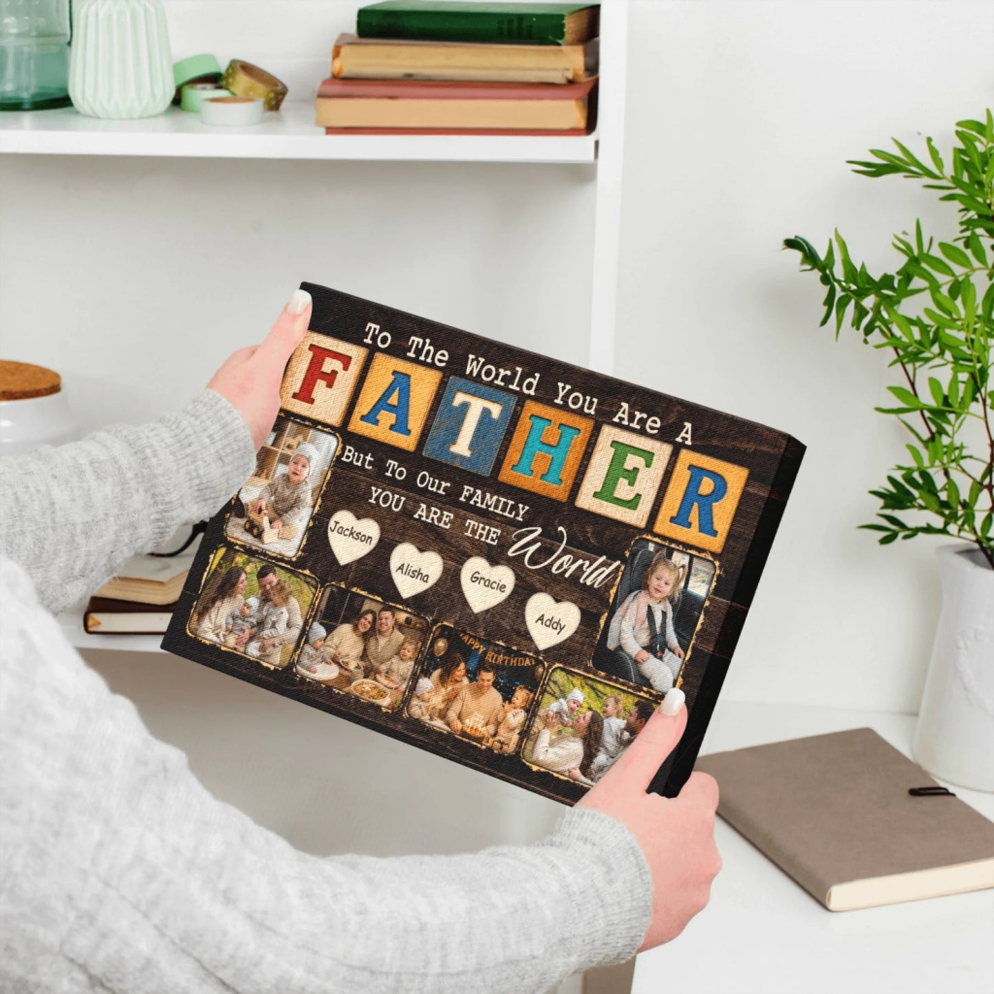 Person holding a personalized photo collage with text 'To the world you are a father, but to our family you are the world' in a home setting.