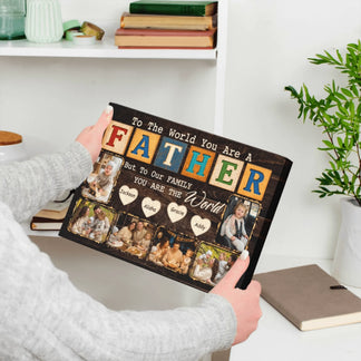 Person holding a personalized photo collage with text 'To the world you are a father, but to our family you are the world' in a home setting.