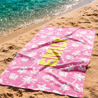 Custom Emily beach towel with a seashell and palm tree theme laid out on the sand by the water for summer.