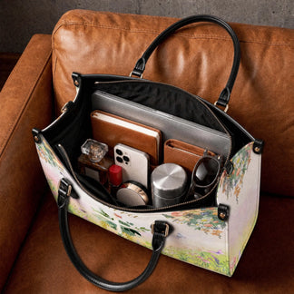 A personalized floral cross tote bag resting on a brown leather couch, filled with a laptop, wallet, phone, and perfume.