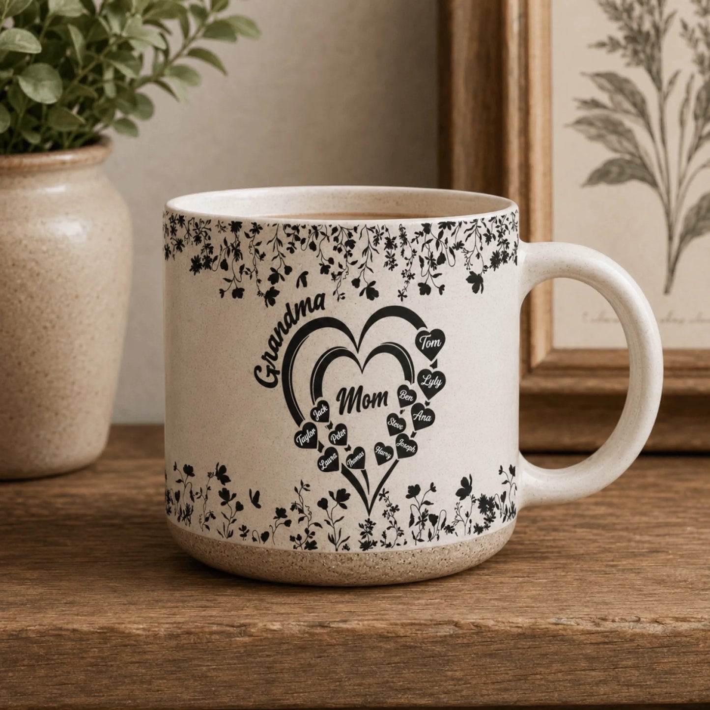 Ceramic mug featuring a floral heart design with Grandma and Mom text and multiple family member names on a wooden shelf.