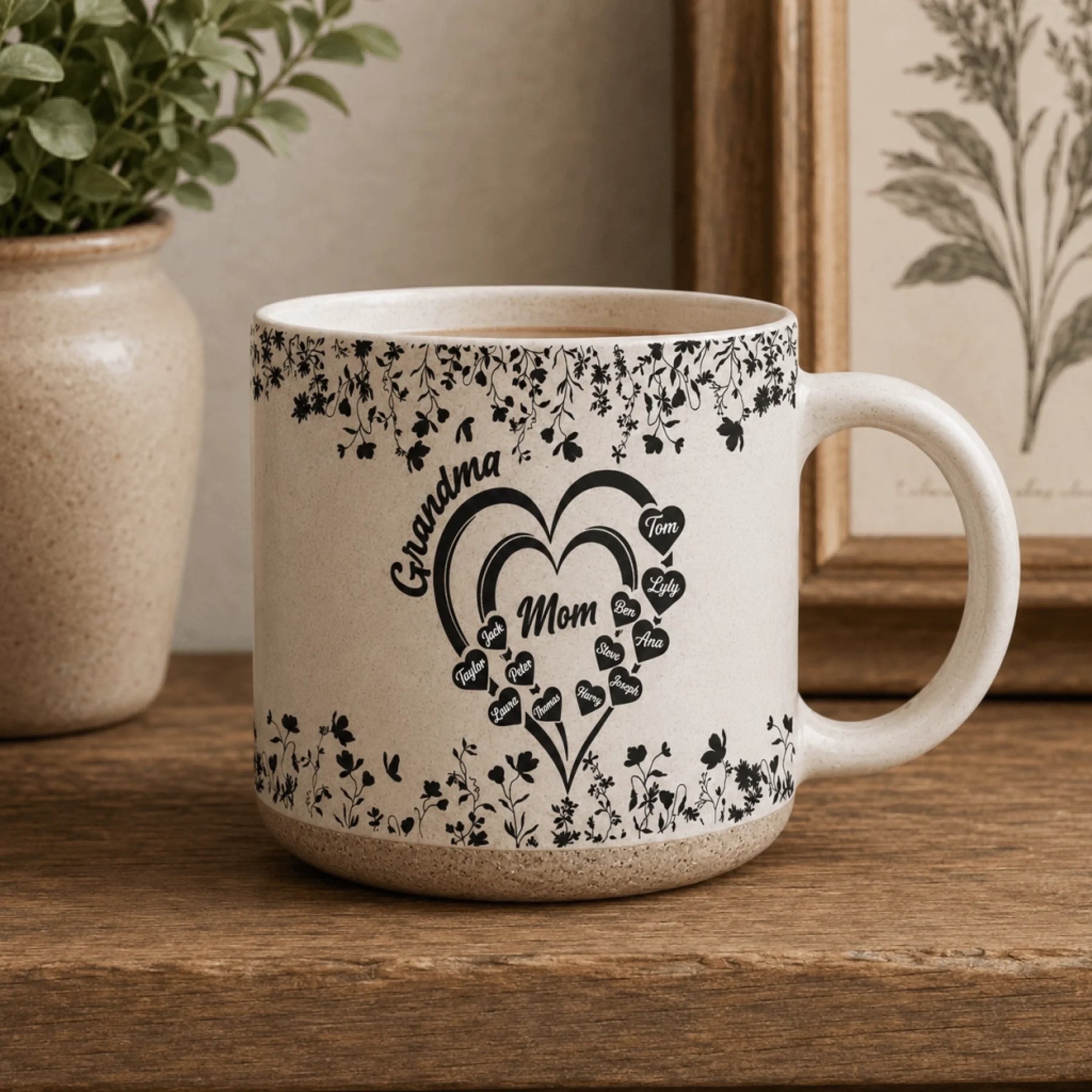 Ceramic mug featuring a floral heart design with Grandma and Mom text and multiple family member names on a wooden shelf.