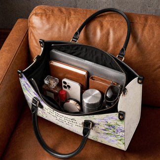 Spacious personalized floral handbag filled with daily items like a laptop, phone, perfume, and wallet on a couch.