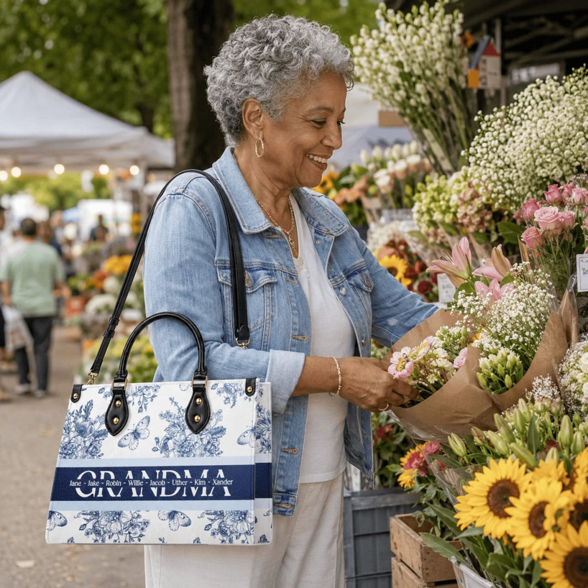 A woman holding a personalized floral tote bag with the name Grandma and custom names while shopping at a flower market.