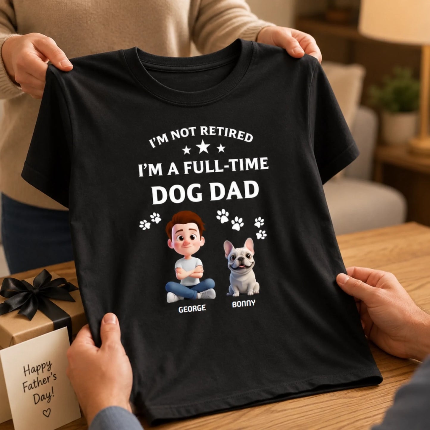 Black t-shirt with 'I'm not retired, I'm a full-time dog dad' text and cartoon characters on a wooden table.