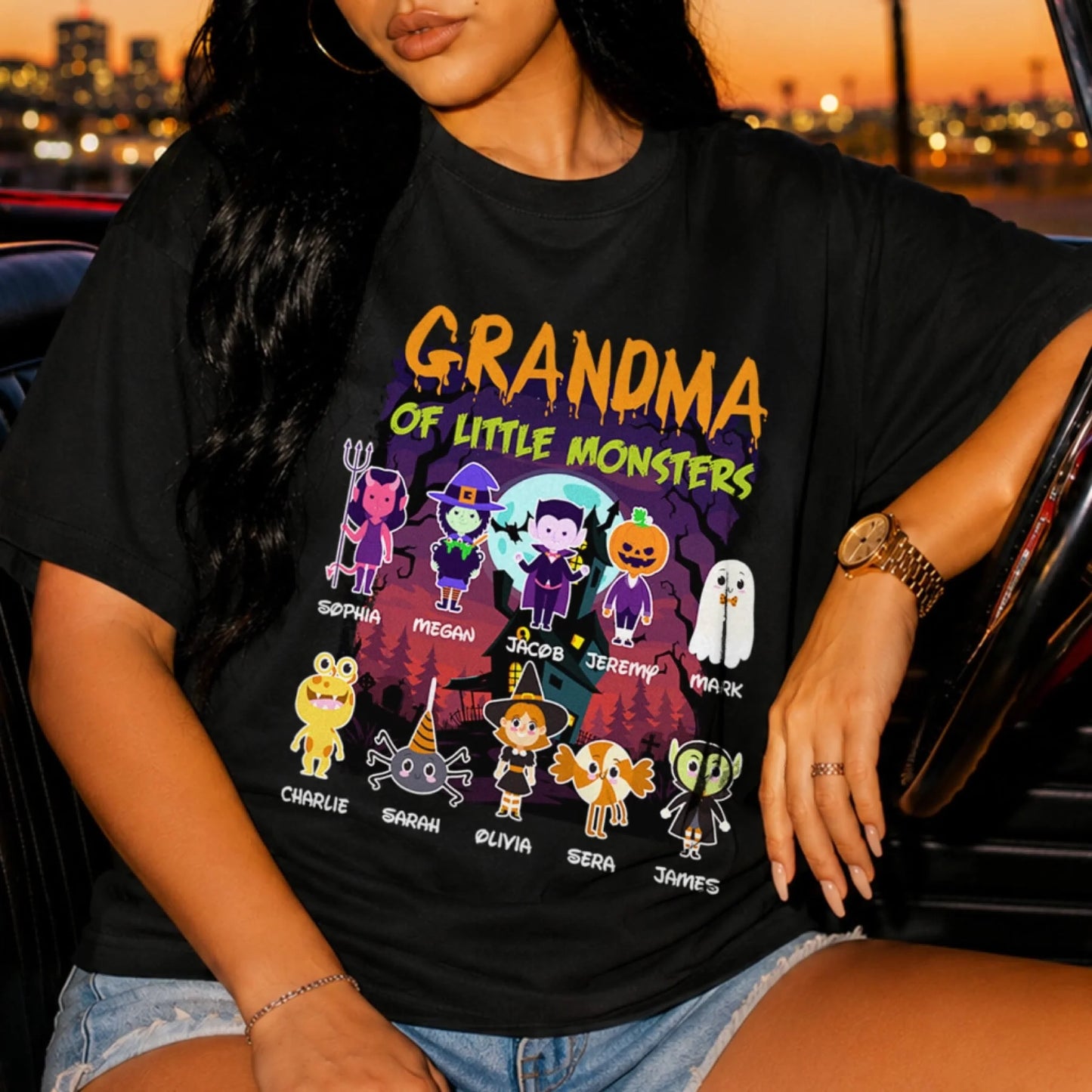 A woman wears a black custom Halloween graphic t-shirt with a Grandma of Little Monsters print and kid names.