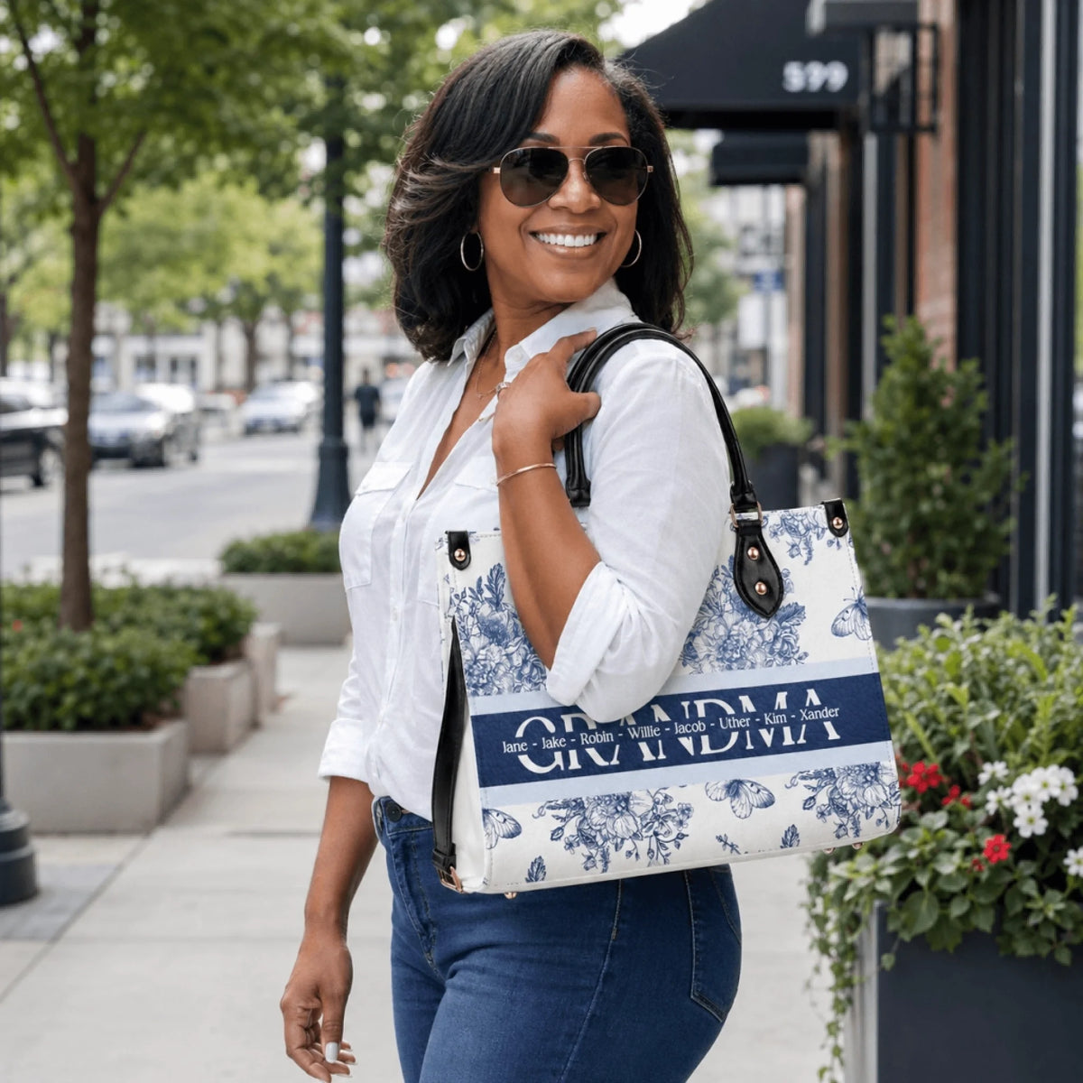 A woman carrying a personalized white tote bag with a blue floral design and the word Grandma featuring custom names.
