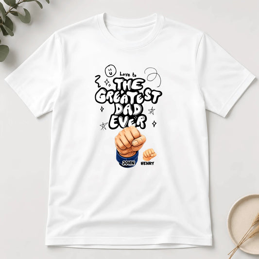 White t-shirt with 'Love is the Greatest Dad Ever' design on a light gray background