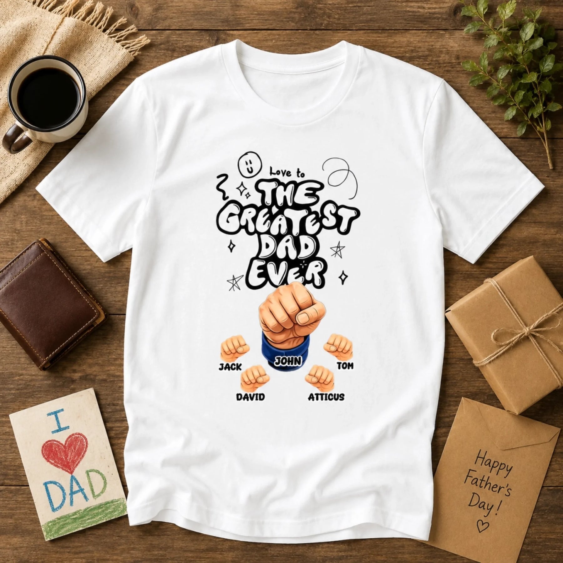 White t-shirt with 'Love is the greatest dad ever' design on a wooden surface with Father's Day items.