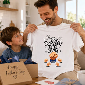 Man holding a t-shirt with 'The Greatest Dad Ever' design, smiling with a child in a home setting.