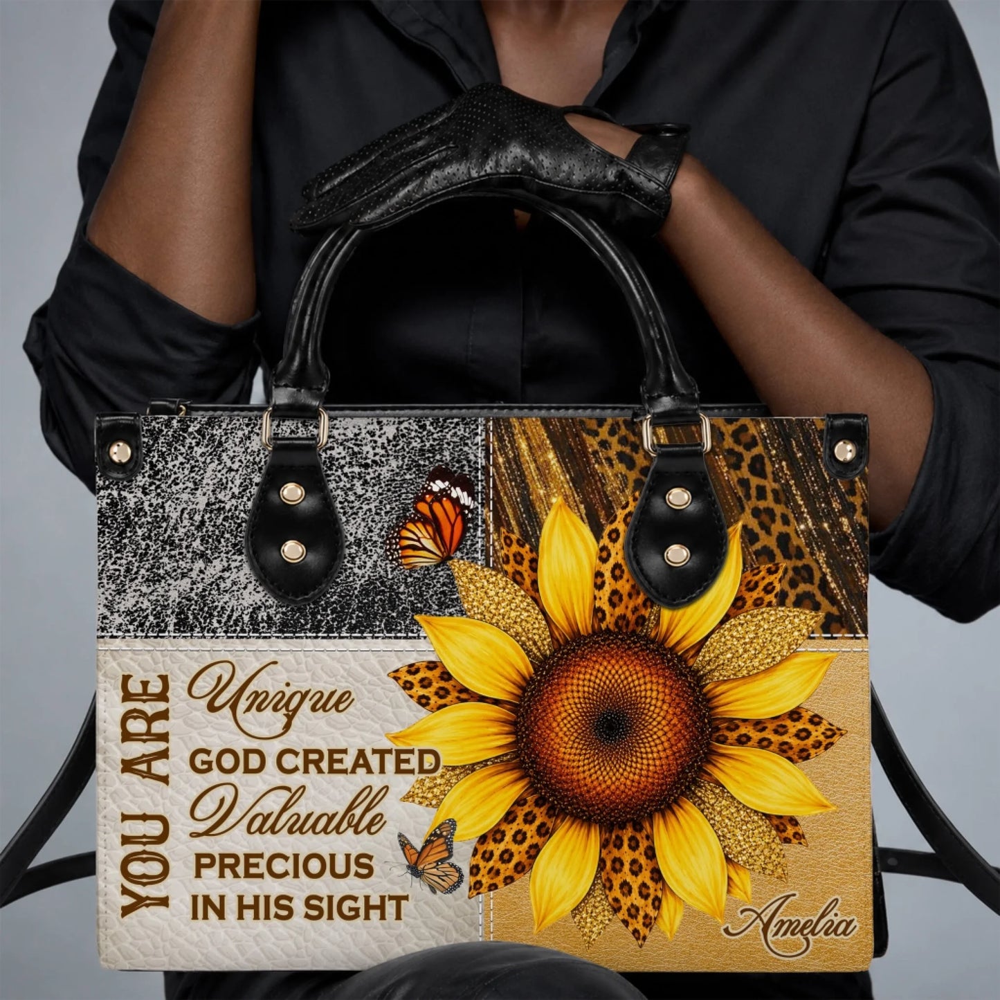 A person wearing black gloves holding a custom sunflower and butterfly tote bag with the name Amelia on the front.