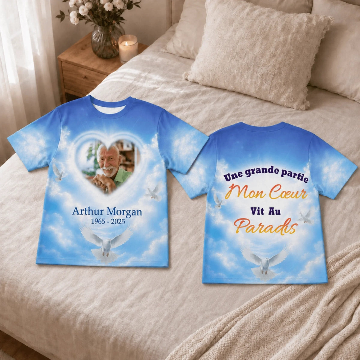 A personalized memorial t-shirt displayed on a bed featuring a custom photo, name, and dates in a heavenly design.