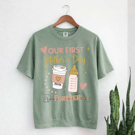 Green t-shirt with 'Our First Mother's Day Forever' graphic on a hanger against a white background.