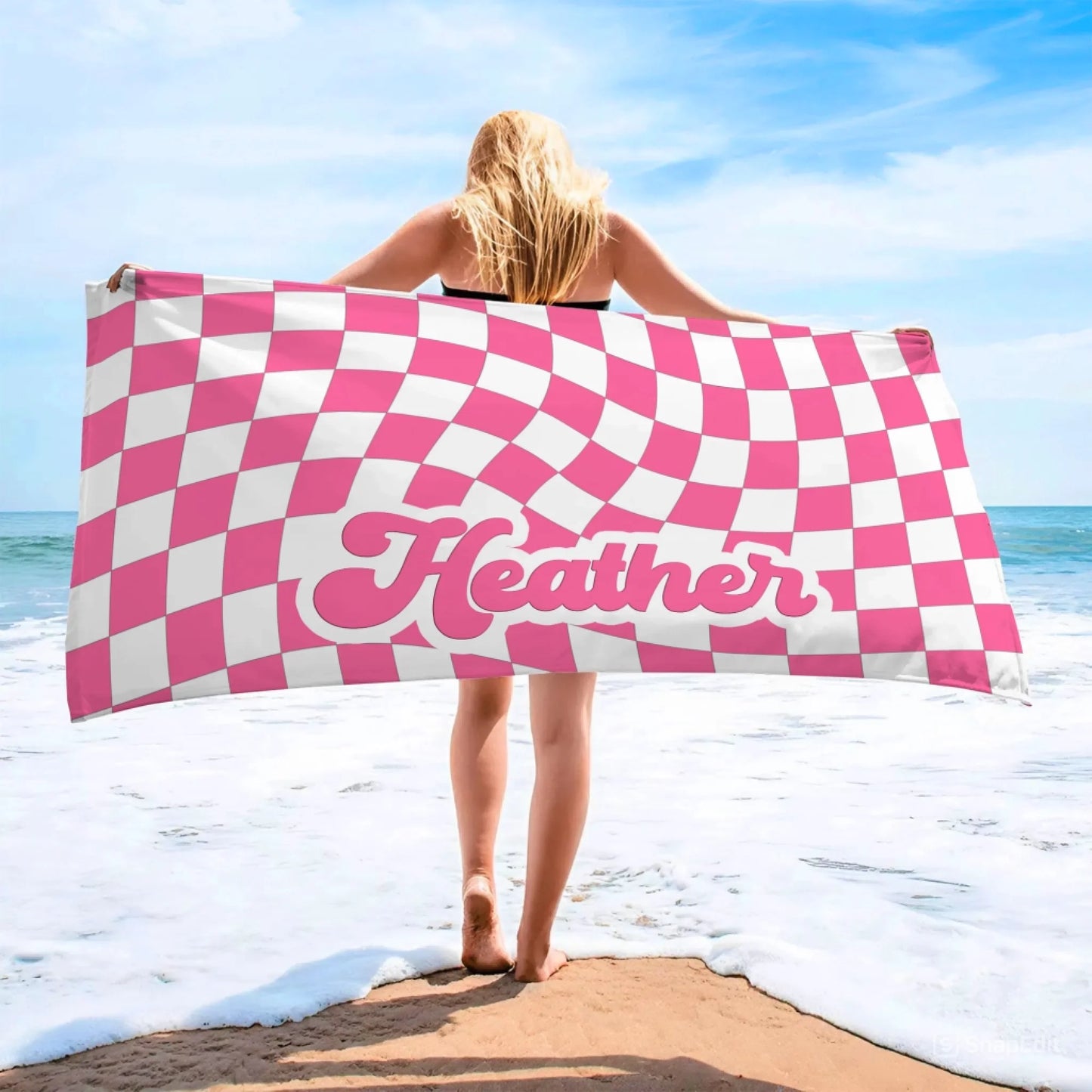 A personalized beach towel featuring a pink and white wavy checkerboard pattern with the name Heather printed in script.