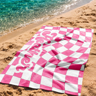 Custom beach towel with a wavy pink checkerboard design and the name Heather displayed on the sandy beach.