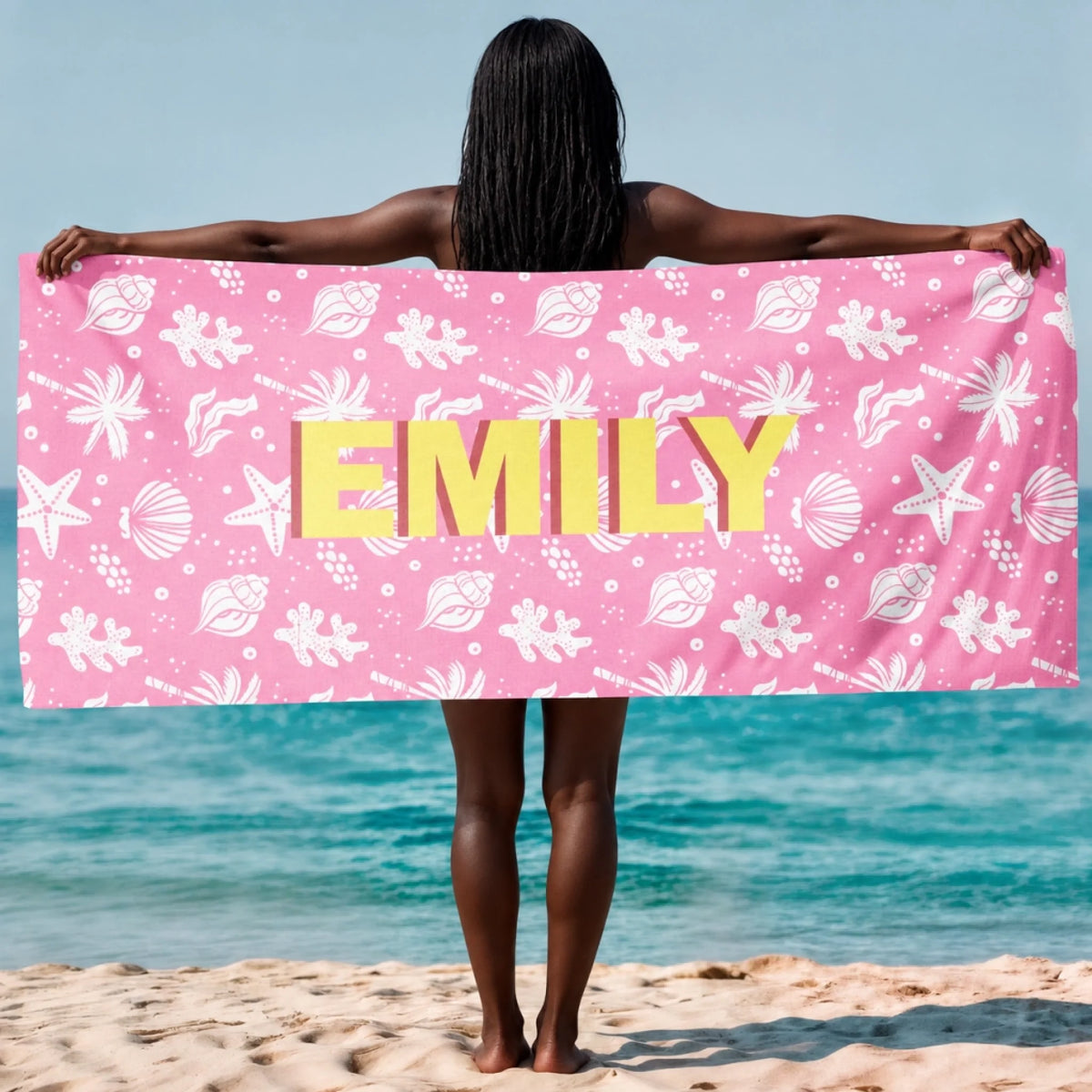 Customized beach towel for Emily with a yellow name print on a soft pink background featuring white seashell patterns.