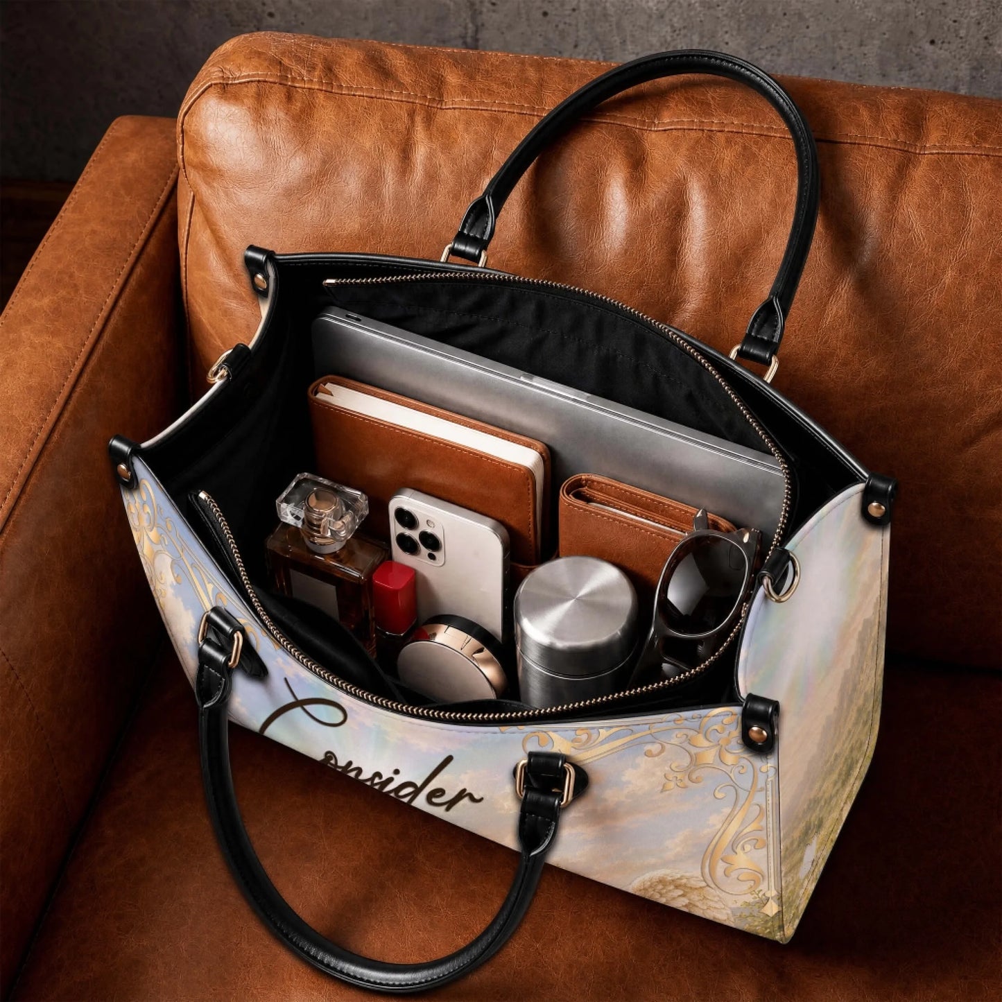 Spacious interior of a custom printed angel handbag showing organized contents like a laptop notebook phone and water bottle.