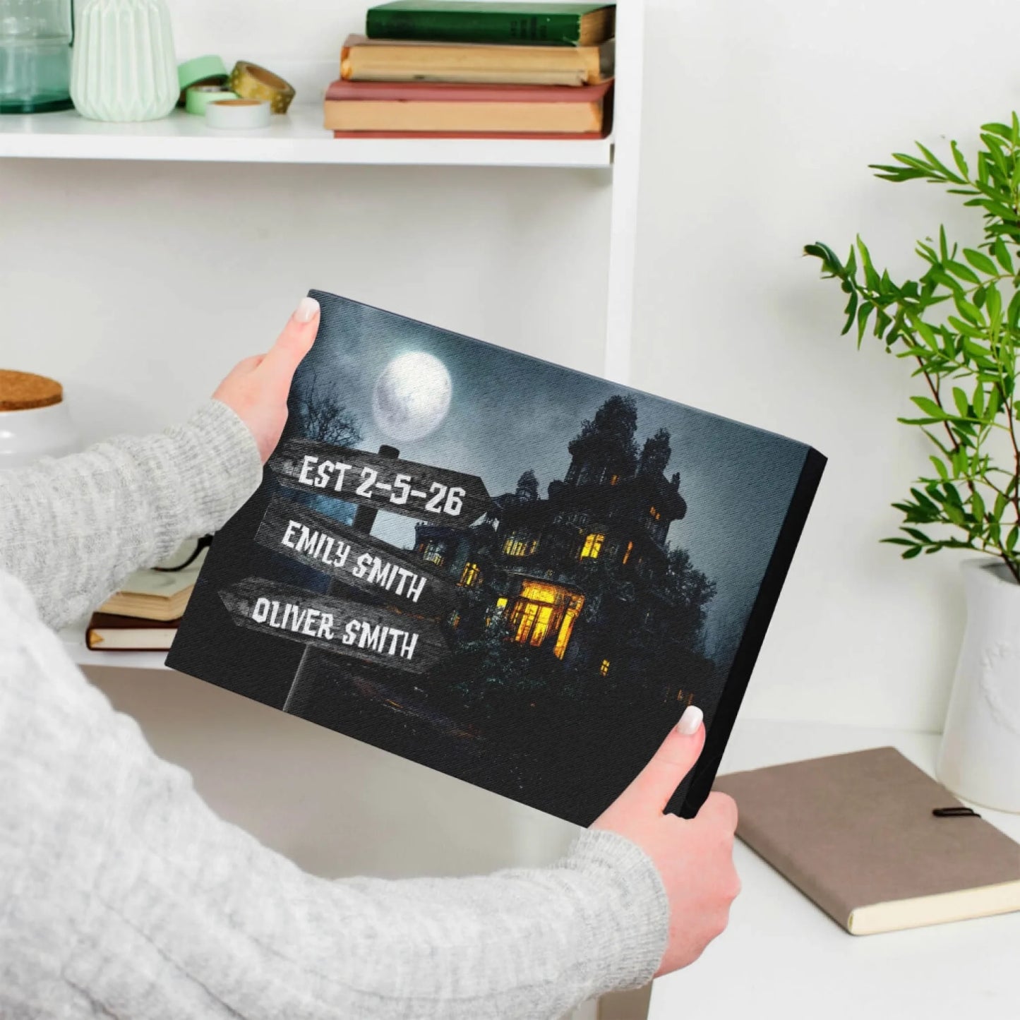 Hands holding a custom haunted house canvas print with names and establishment date perfect for Halloween decor.