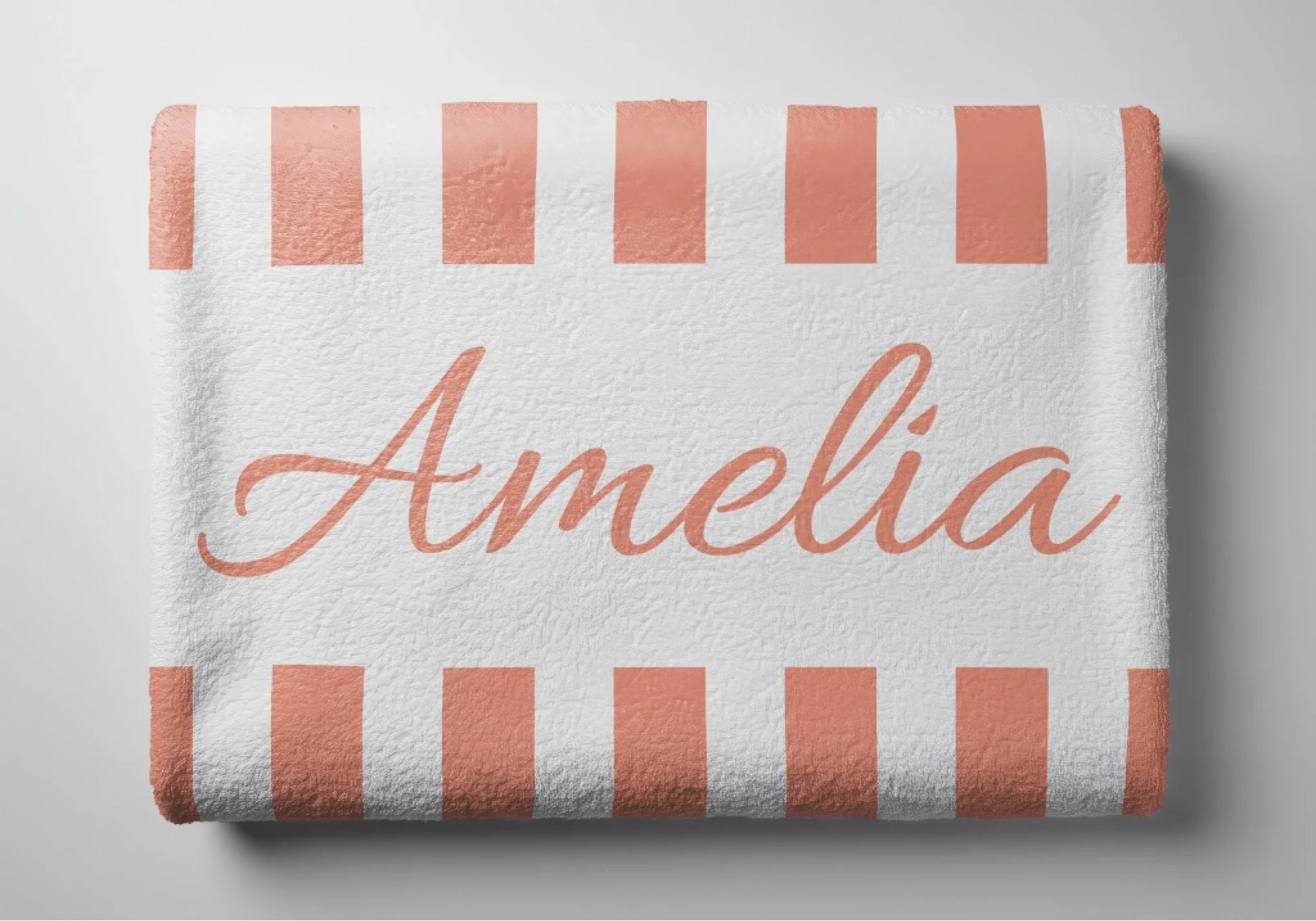Folded peach and white striped beach towel featuring the personalized name Amelia in a cursive script font style.