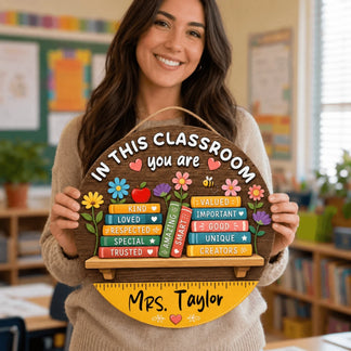 Teacher holding a custom round wooden classroom sign with book stack design featuring positive quotes and teacher name
