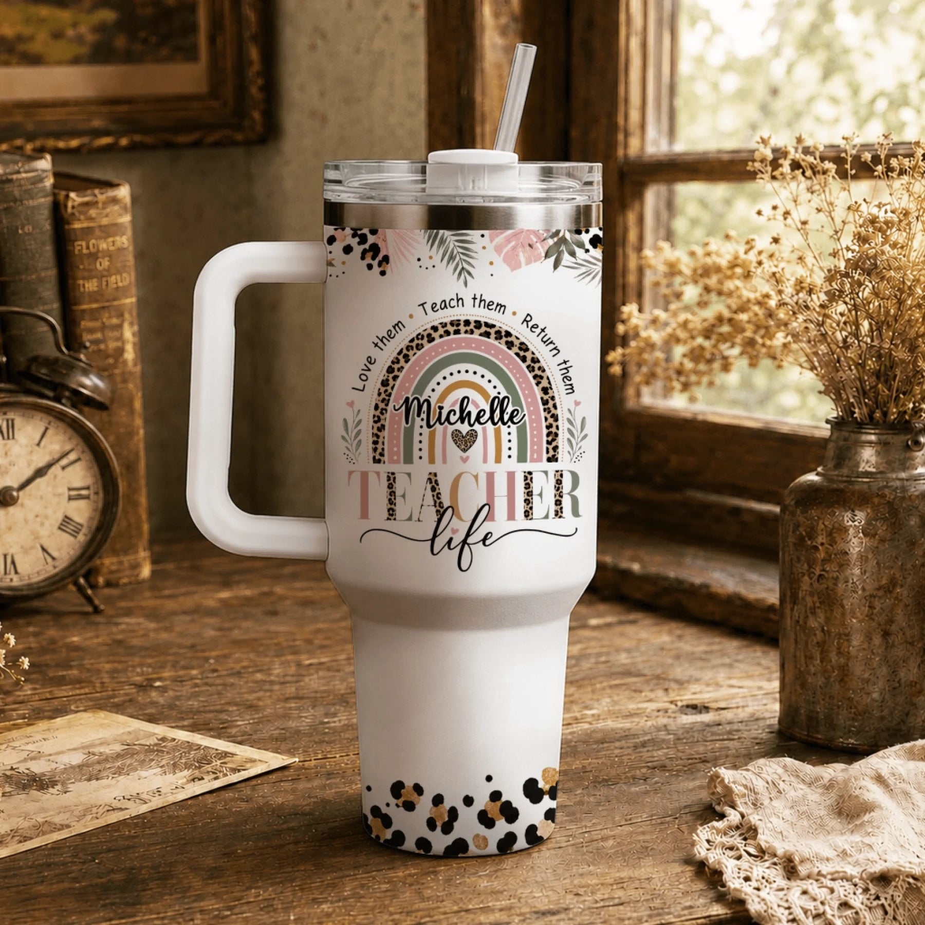 Stainless steel teacher tumbler with personalized name and leopard rainbow art displayed on a rustic wooden desk.