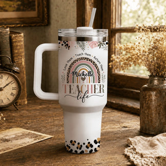 Stainless steel teacher tumbler with personalized name and leopard rainbow art displayed on a rustic wooden desk.