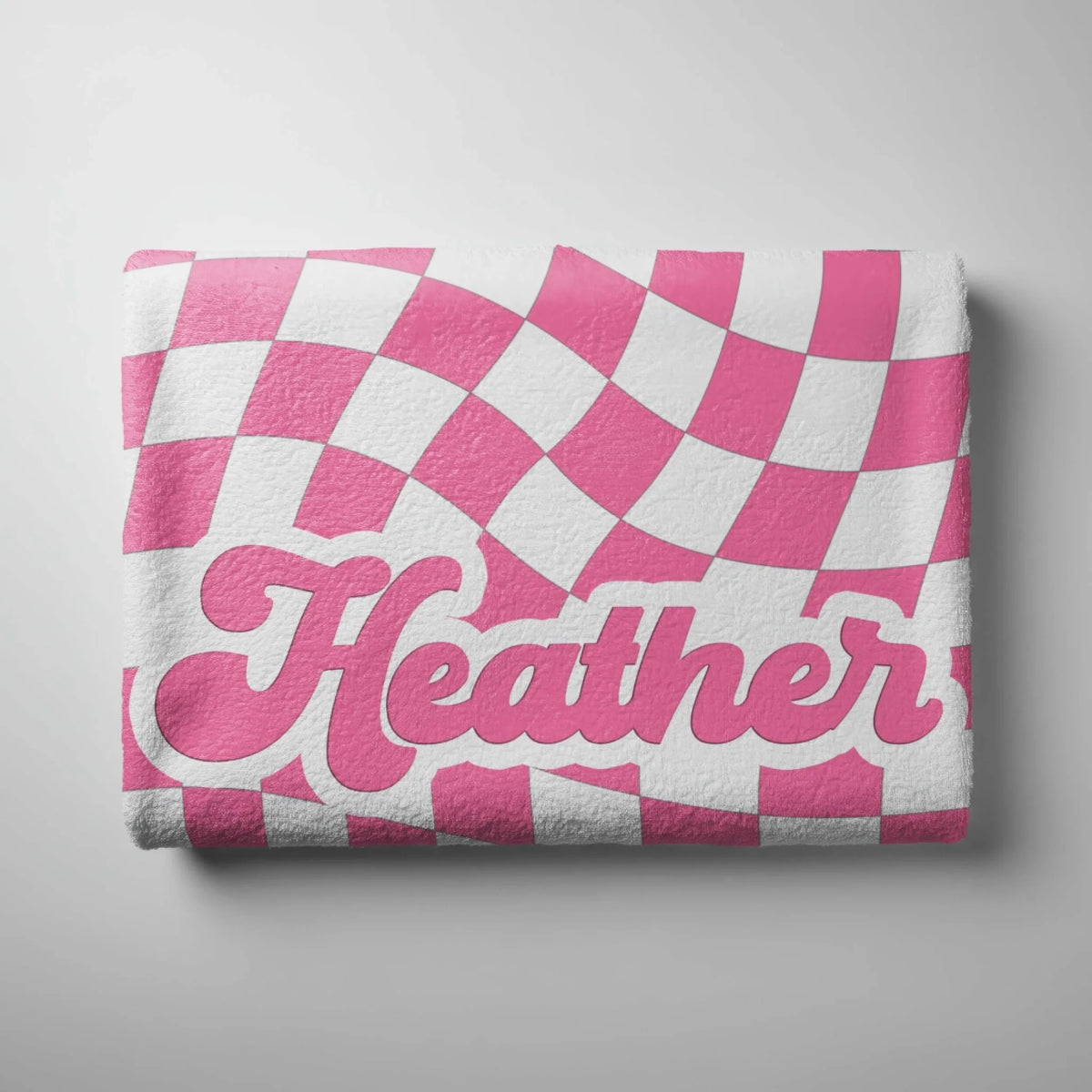 Folded personalized beach towel with a wavy pink and white checkerboard pattern and the custom name Heather.