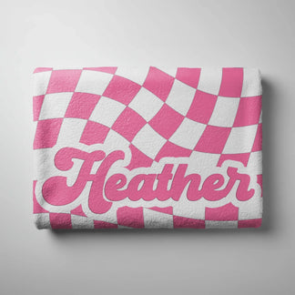 Folded personalized beach towel with a wavy pink and white checkerboard pattern and the custom name Heather.