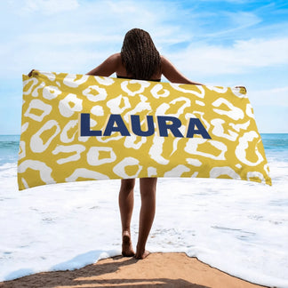 Customized beach towel featuring the name Laura in bold blue text on a yellow and white animal print background.