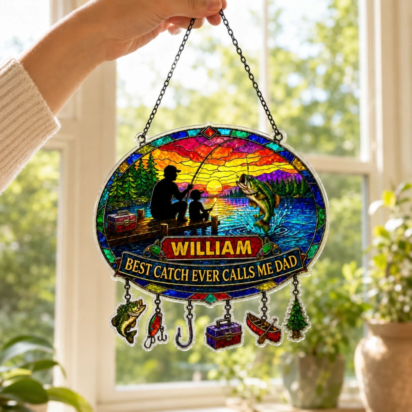 Decorative stained glass panel with fishing design and text, held in front of a window.