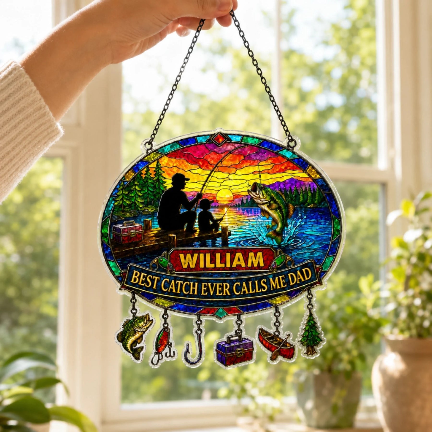Decorative stained glass panel with fishing design and text, held in front of a window.