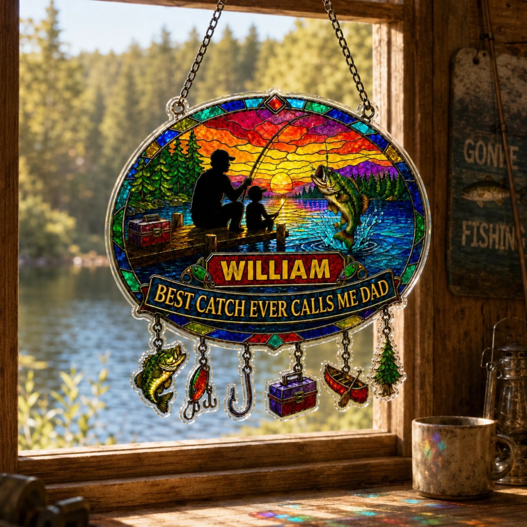 Stained glass panel with fishing scene and 'William' name, hanging by a window with a view of a lake.