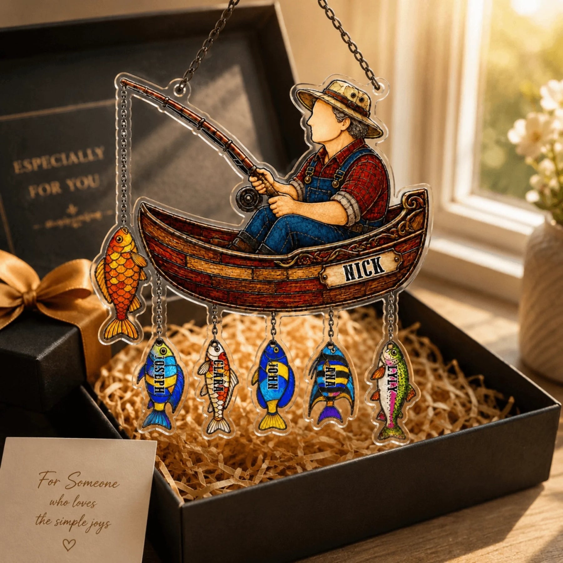 Decorative hanging ornament with a fisherman in a boat and colorful fish, placed in a box.