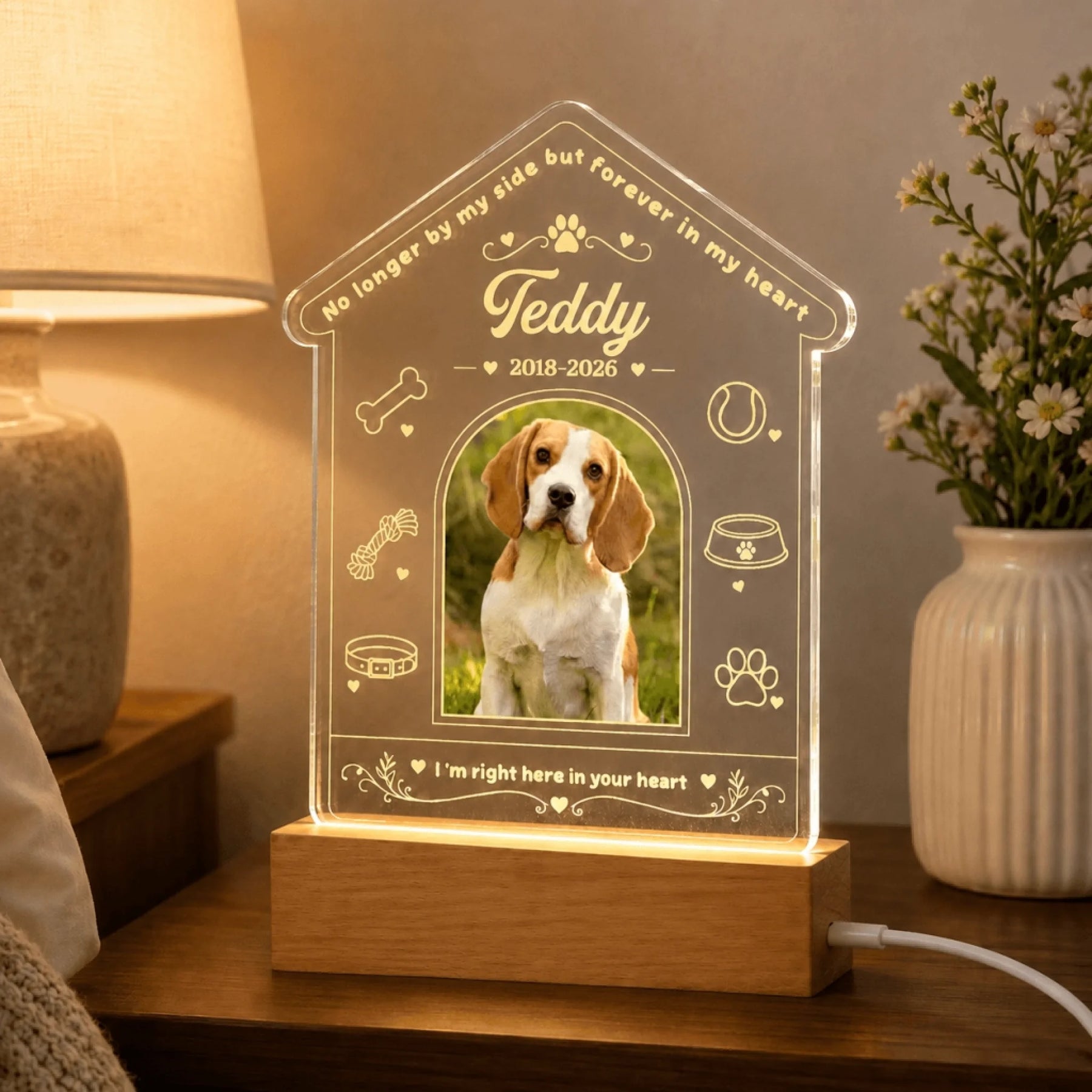 Glowing custom acrylic pet memorial lamp featuring dog-themed icons and a photo on a wooden base on a bedside table.