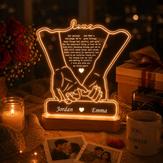 A glowing acrylic lamp featuring clasped hands, a heartfelt quote, and names "Jordan" and "Emma" amidst roses, a camera, and photos.