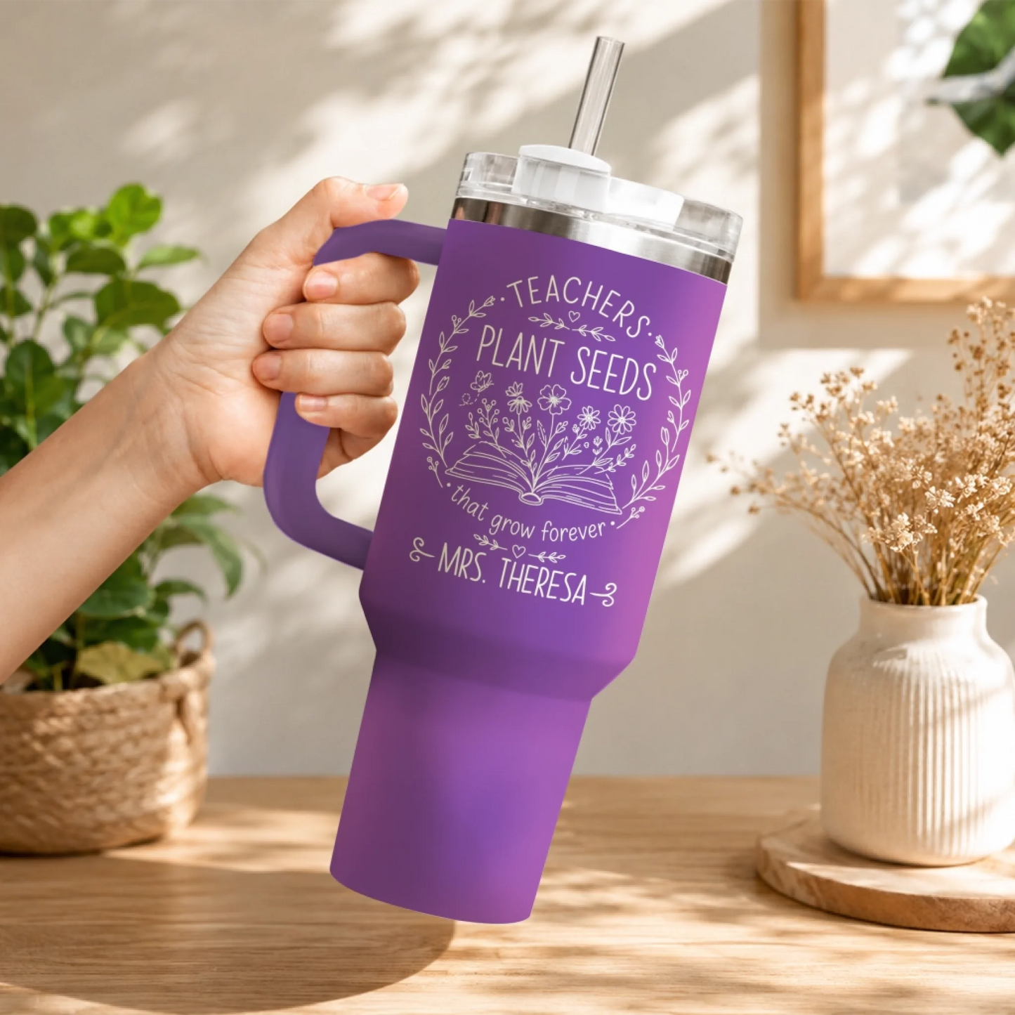 Close-up hand holding a purple stainless steel teacher tumbler with personalized floral book design.