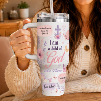 Close-up view of a Christian-themed tumbler held by a woman in a beige sweater, showing floral prints and scripture text.