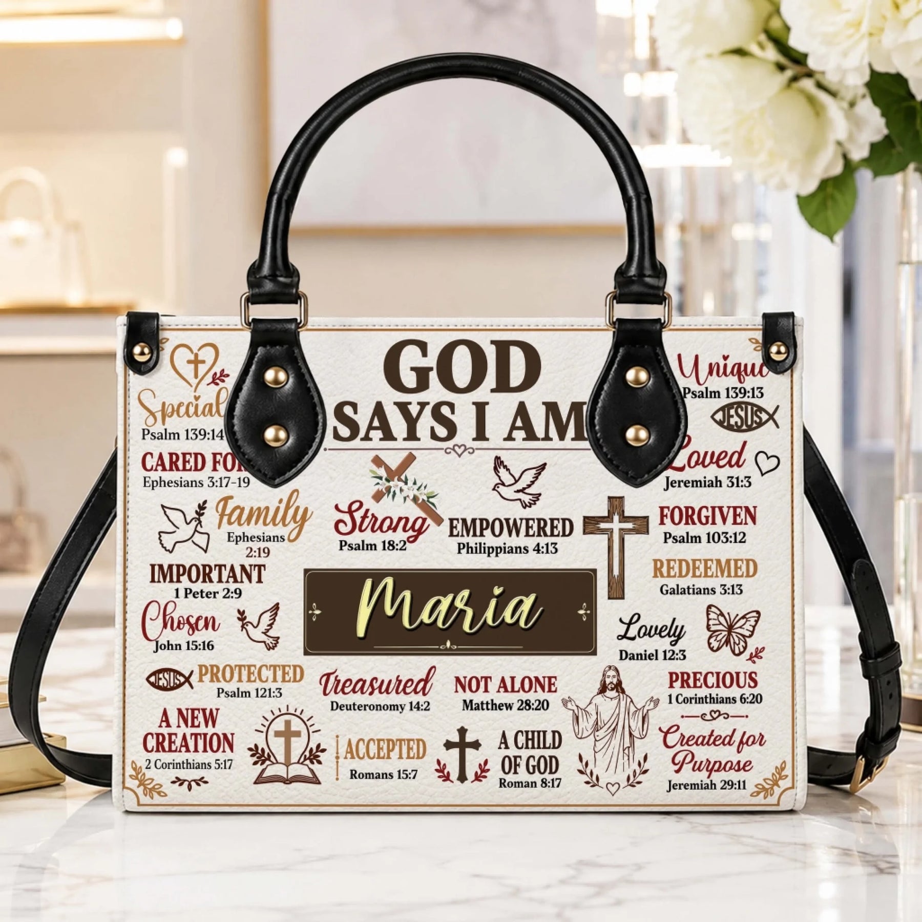 A stylish religious handbag on a marble table, printed with the text God Says I Am and the custom name Maria.