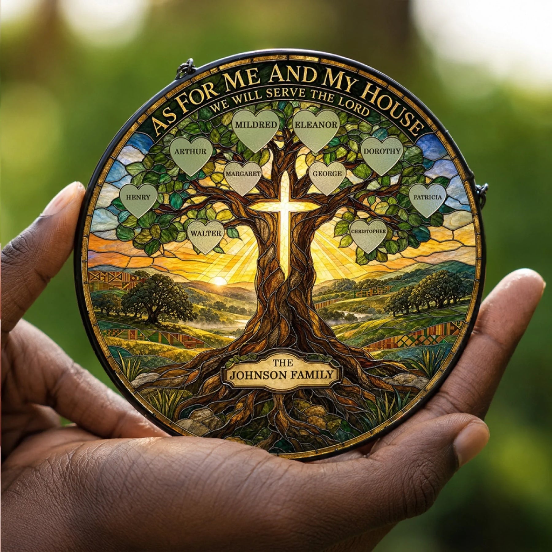 Person holding a religious tree of life stained glass suncatcher with custom family names in hearts against a sunrise background.