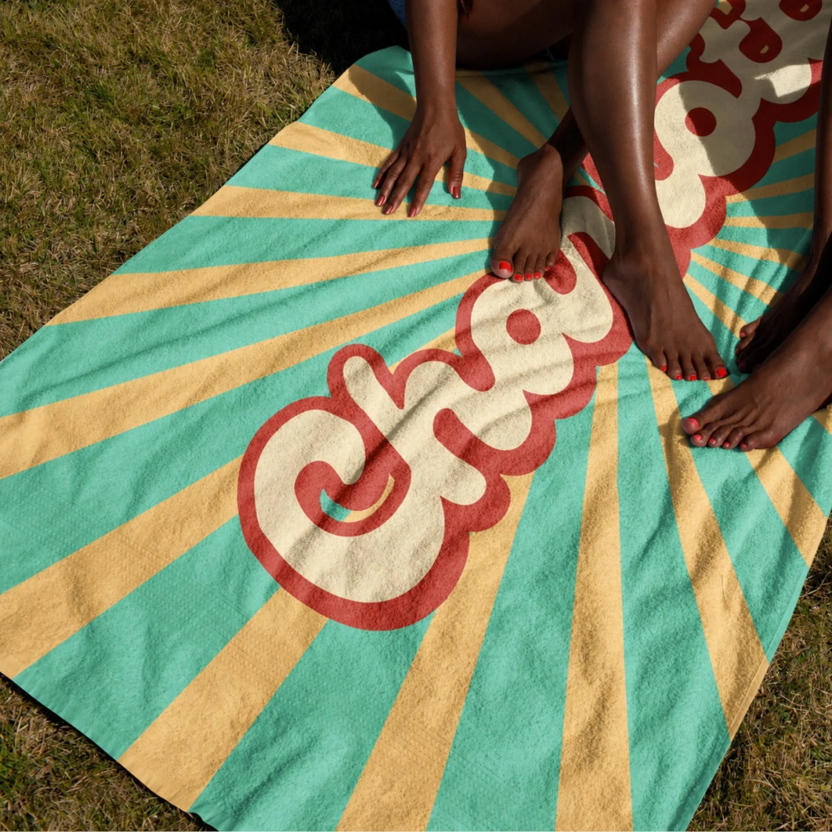 Close up of a personalized beach towel with retro sunburst design and custom name resting on green summer grass.