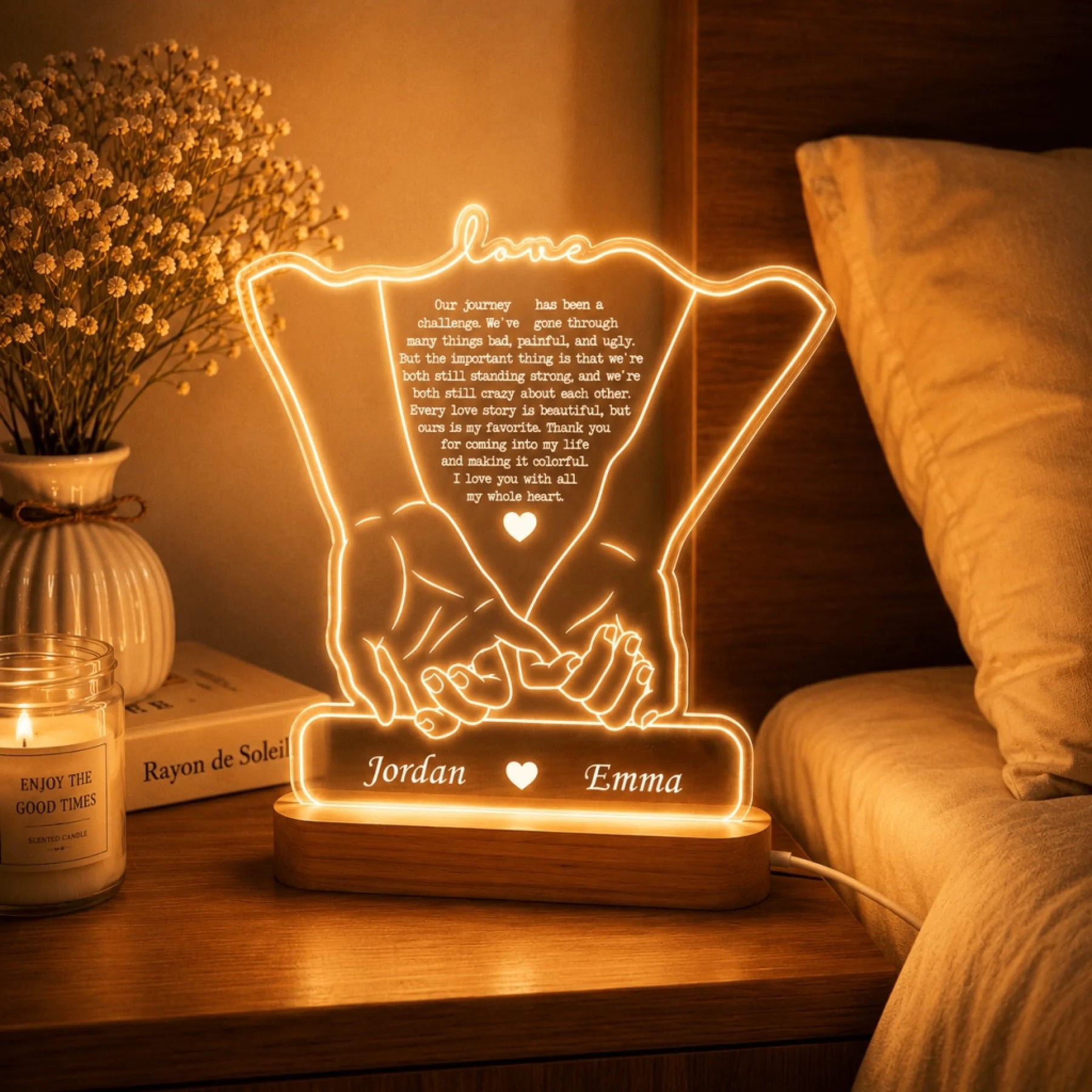 An illuminated lamp with an outline of holding hands, a romantic quote, and names "Jordan" and "Emma" on a bedside table.