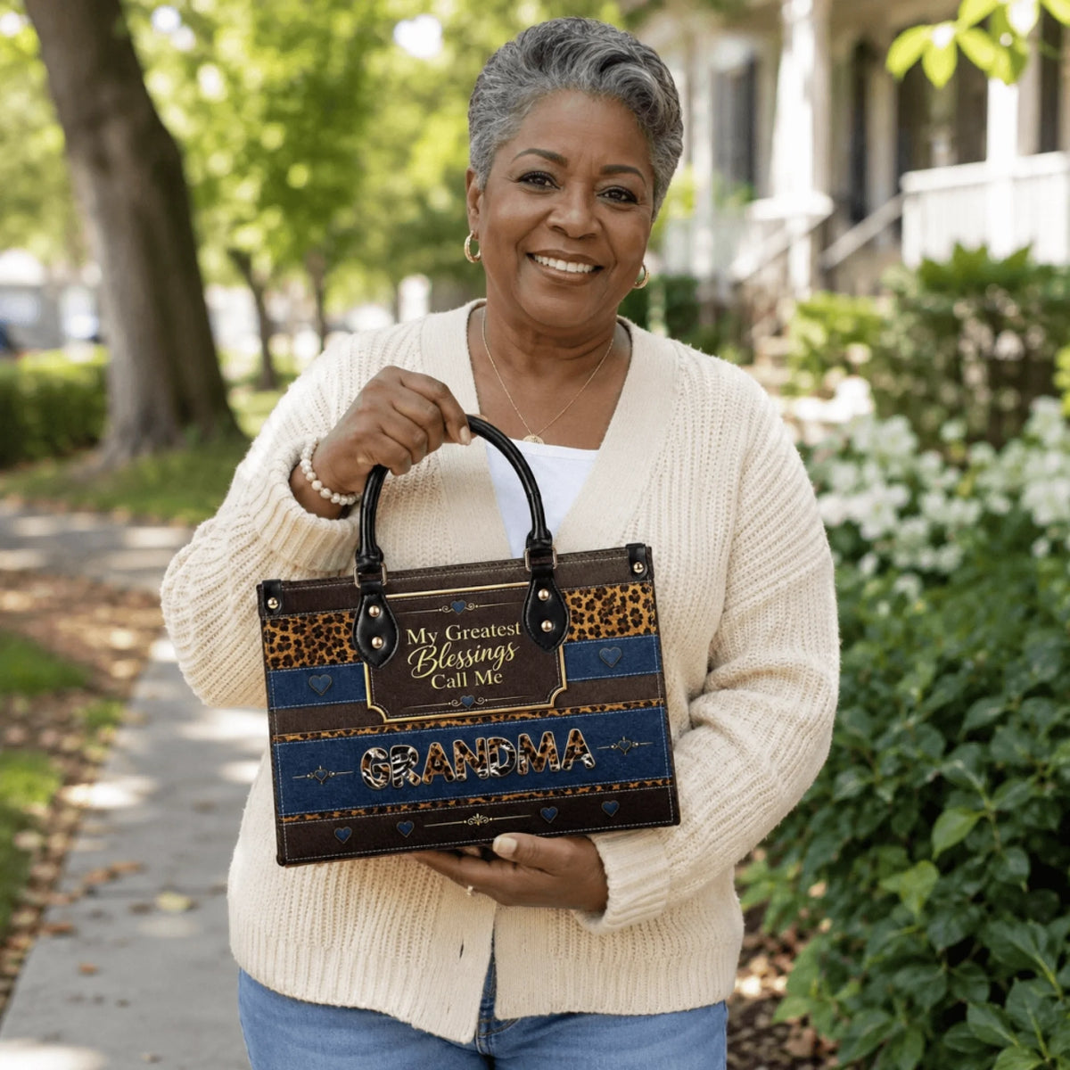 A smiling grandmother holding a custom-designed handbag with animal print accents and the text My Greatest Blessings.